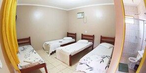 Une chambre avec quatre lits simples, une petite fenêtre et une salle de bain équipée de toilettes et d’une douche.