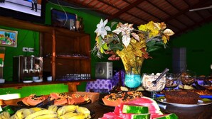 Ein reichhaltiges Buffet mit verschiedenen Früchten und Desserts, eine dekorative Vase und ein Fernseher im Hintergrund.