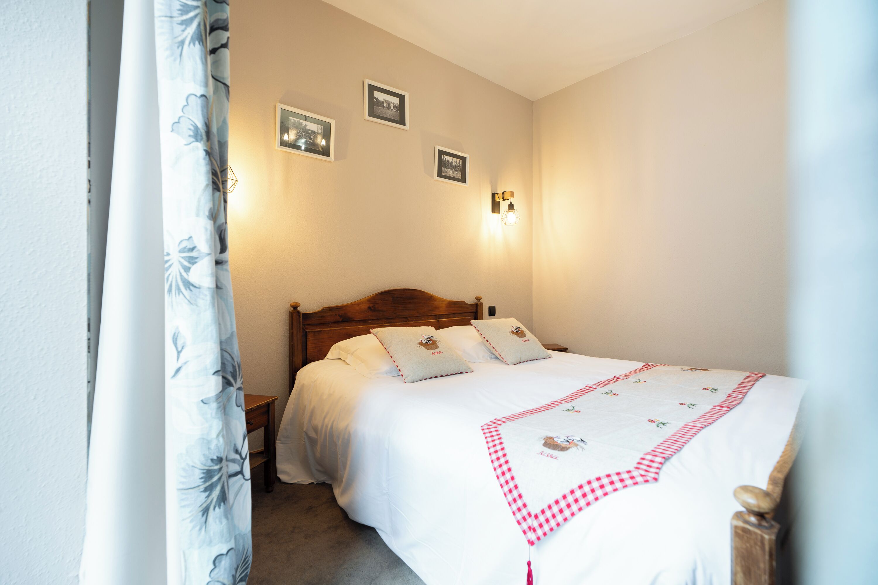 A neatly made bed with a checkered bedspread, two pillows, and a headboard. There are three framed pictures on the wall and a wall-mounted light fixture.