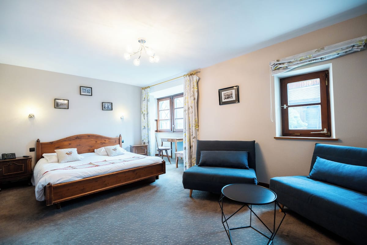 A bedroom with a wooden bed, a blue sofa, a small round table, and a desk with a chair.
