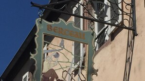 A building with a sign that reads "BERCEAU du Vigneron" and features a man working on a vine.