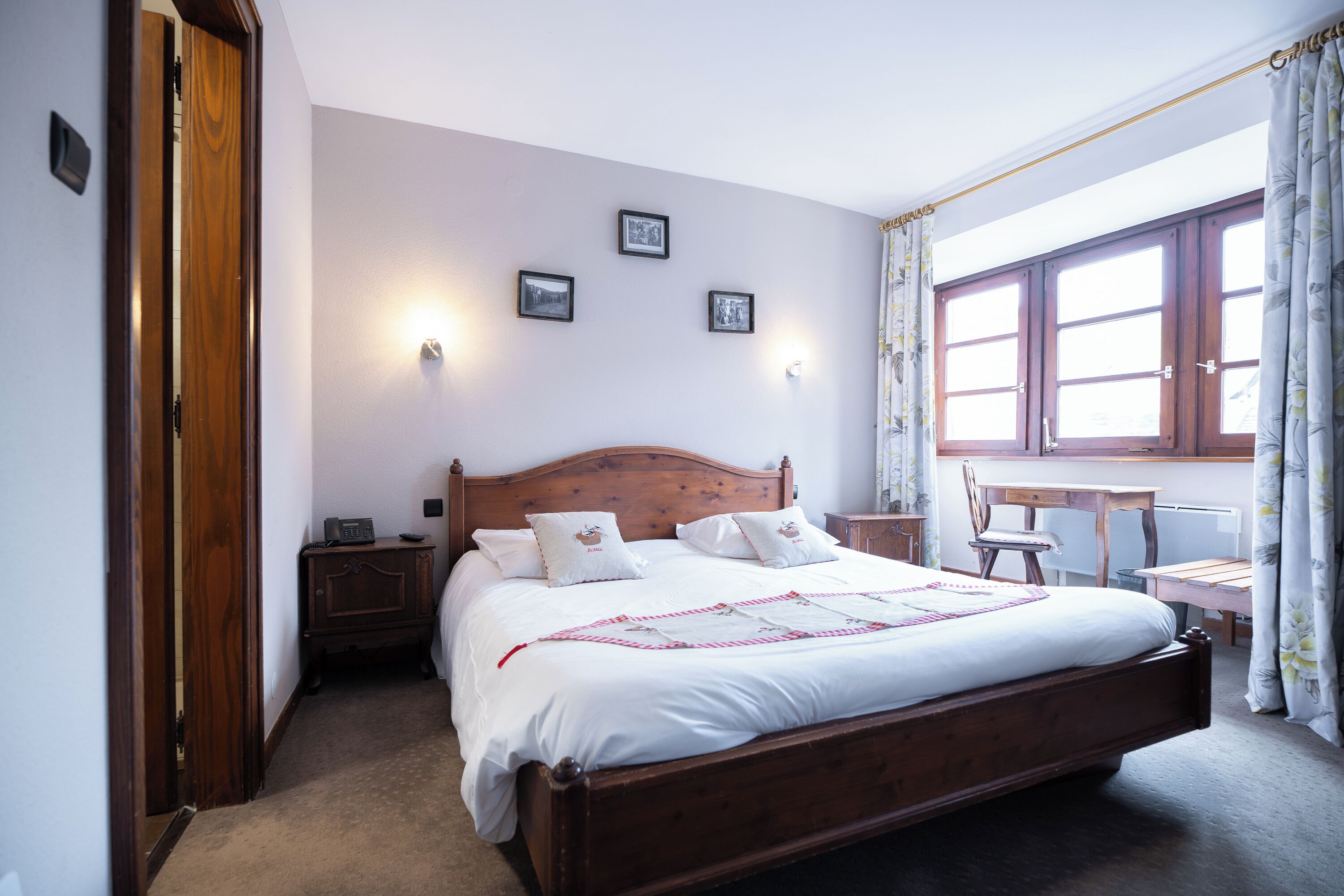 Un dormitorio con una cama de madera, un escritorio y una silla. Hay tres cuadros en la pared.