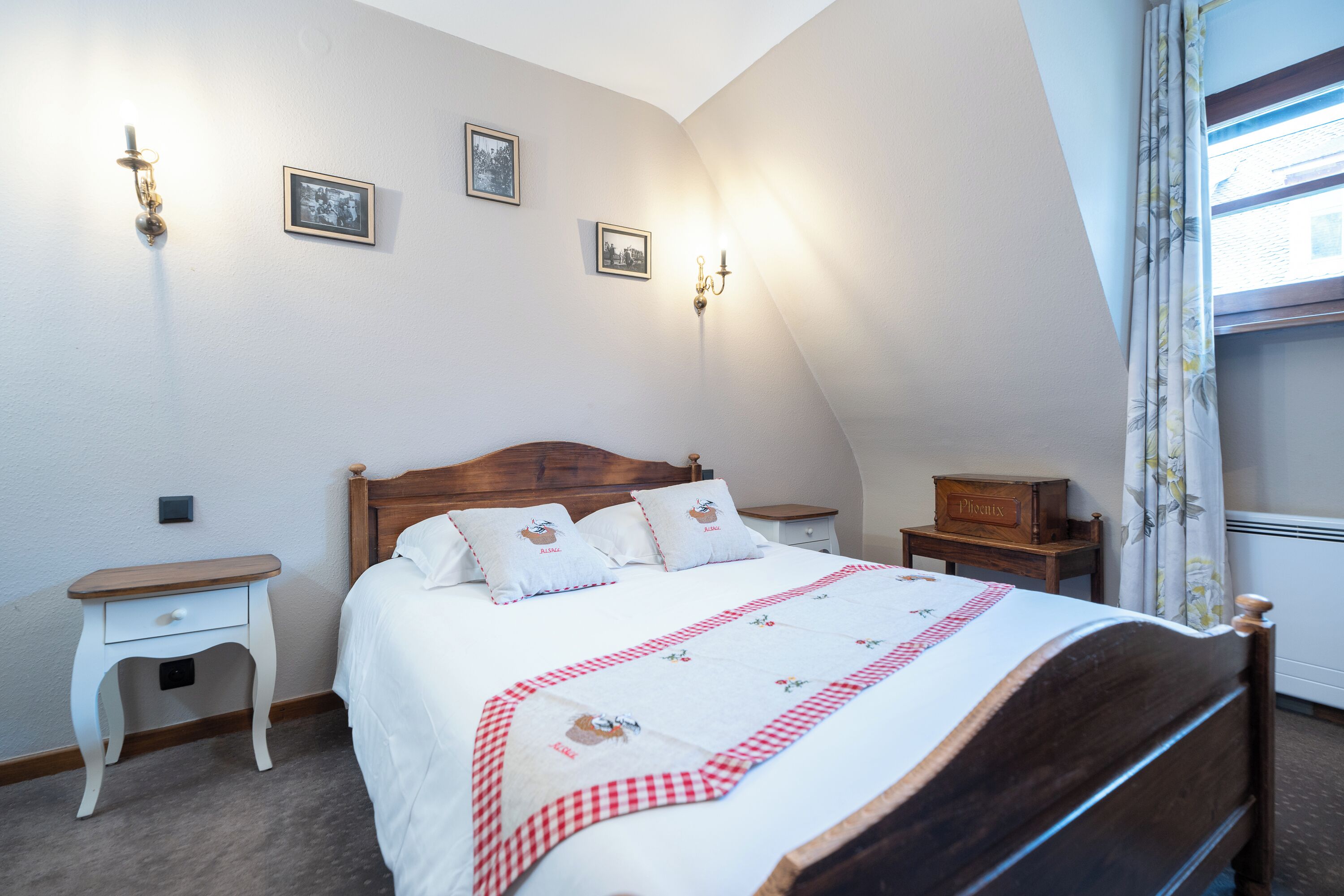 A bedroom with a wooden bed, white bedding, a checkered throw, bedside tables, and wall-mounted lights.