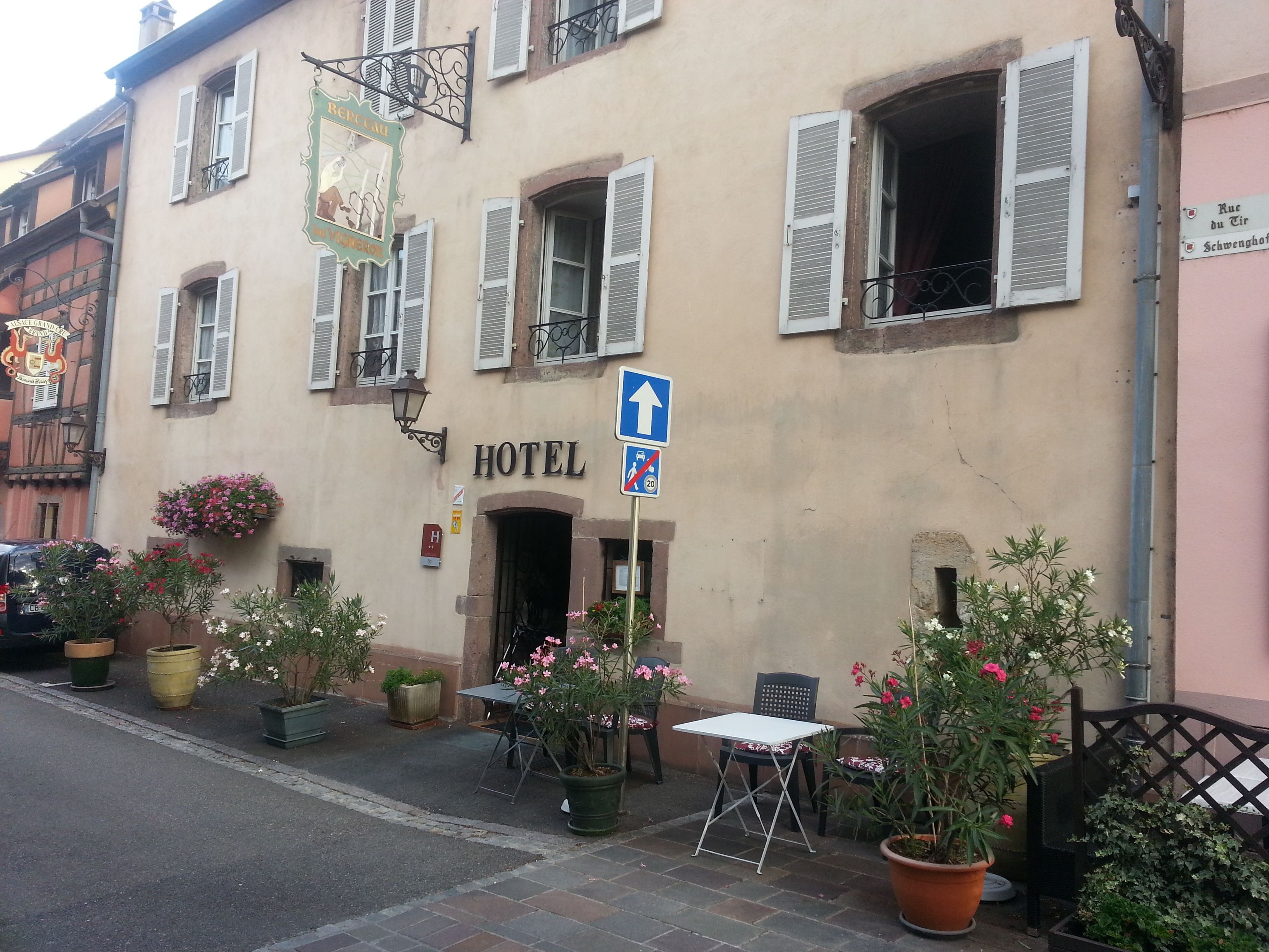 Un hotel con letrero, mesas al aire libre y plantas en macetas.