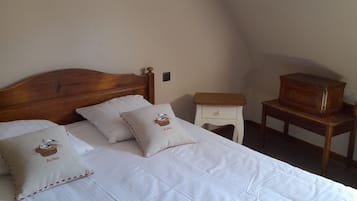 A bedroom with a wooden bed, white bedding, two pillows with a bird design, a nightstand, a dresser, and a wall-mounted lamp.