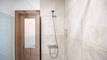 A shower area with a handheld showerhead and a wall-mounted faucet, a wooden door, and a tiled wall with a blue pattern on one side.