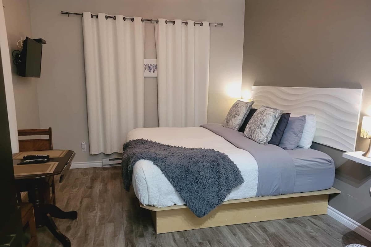 Un dormitorio con cama, una mesita de noche con lámpara, una silla y televisión montada en la pared.