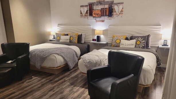 A hotel room with two beds, a black leather armchair, a wooden floor, and a wall art piece above the beds. - Bed & Breakfast Du Repos (Saint Quentin)