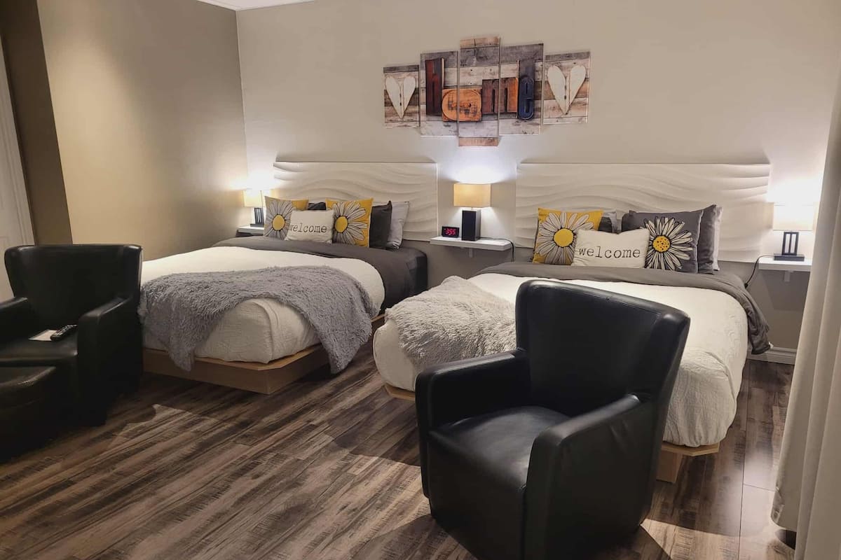 Habitación de hotel con dos camas, un sillón de cuero negro, suelo de madera y una obra de arte sobre las camas.