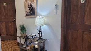 A hallway with wooden flooring, a wooden console table with a lamp, a framed picture, and two doors labeled with numbers. - Bed & Breakfast Du Repos (Saint Quentin)