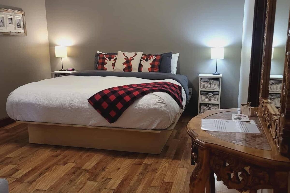 Un dormitorio con cama, dos mesitas de noche con lámparas, suelo de madera, ventilador de techo y un espejo.