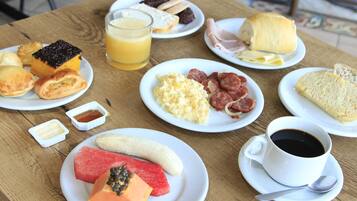 Una mesa de desayuno con diversos alimentos, como huevos, salchichas, tostadas y un vaso de jugo de naranja.