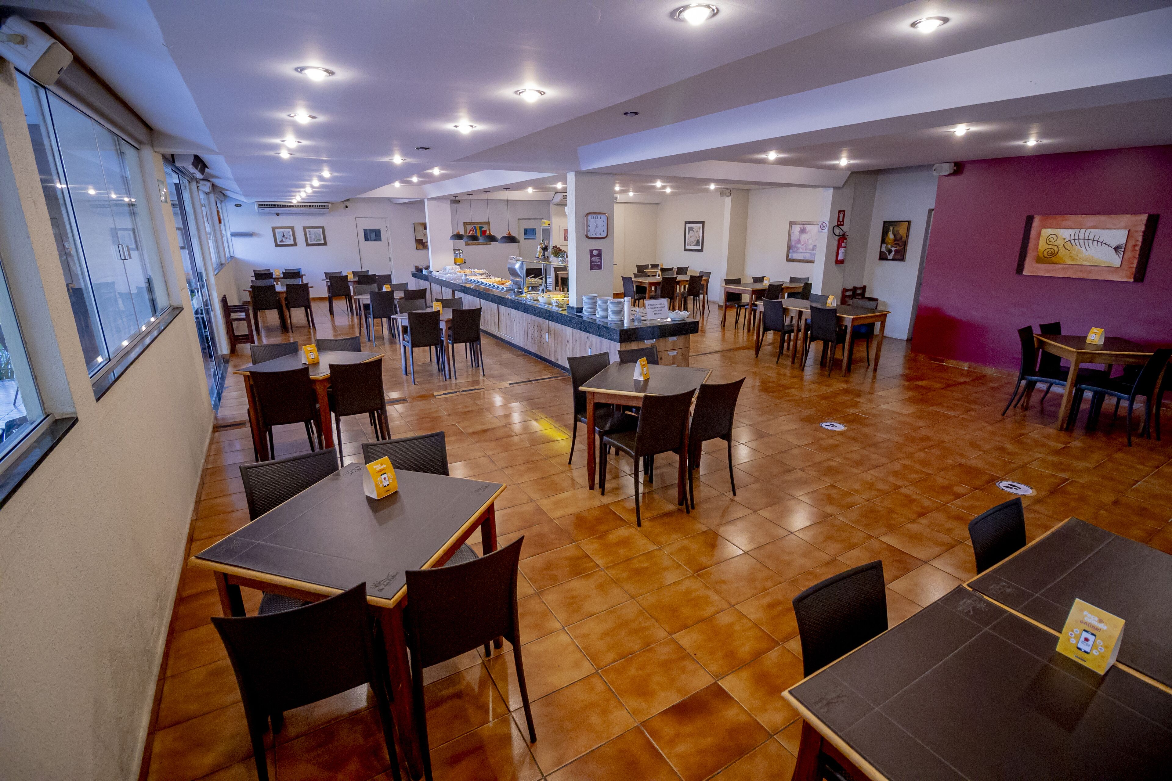 En rymlig restaurang med många bord och stolar, en central disk och utsikt genom stora fönster.
