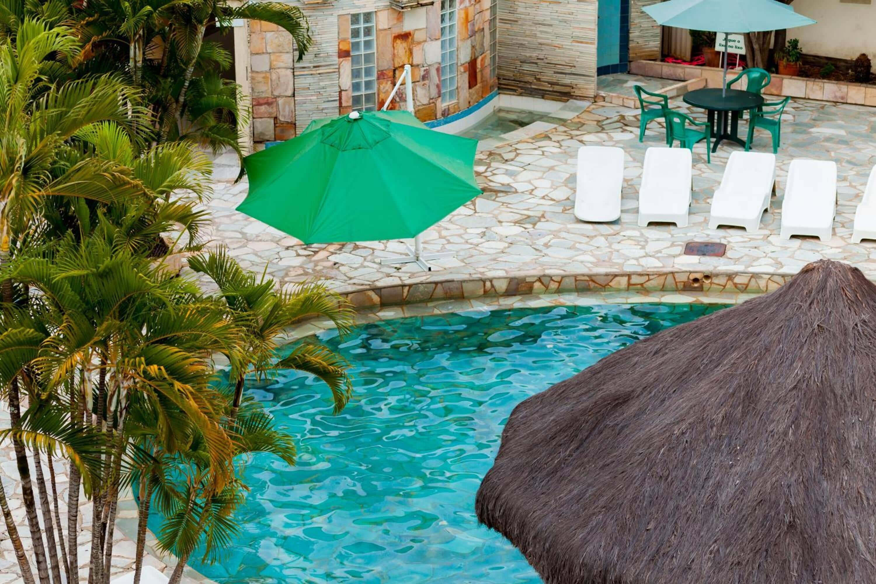 A pool area with lounge chairs, a green umbrella, and palm trees.