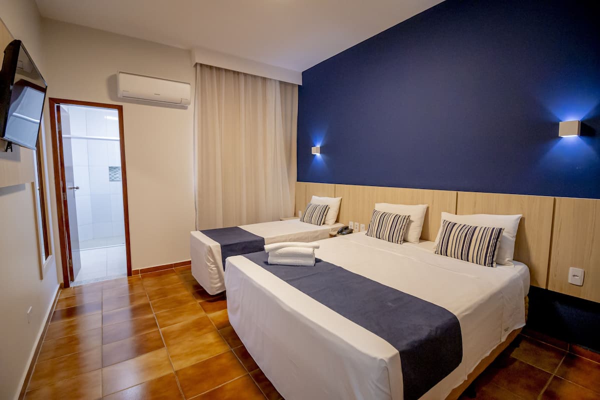 A hotel room with two beds, a large mirror, an air conditioning unit, and a TV on the wall.