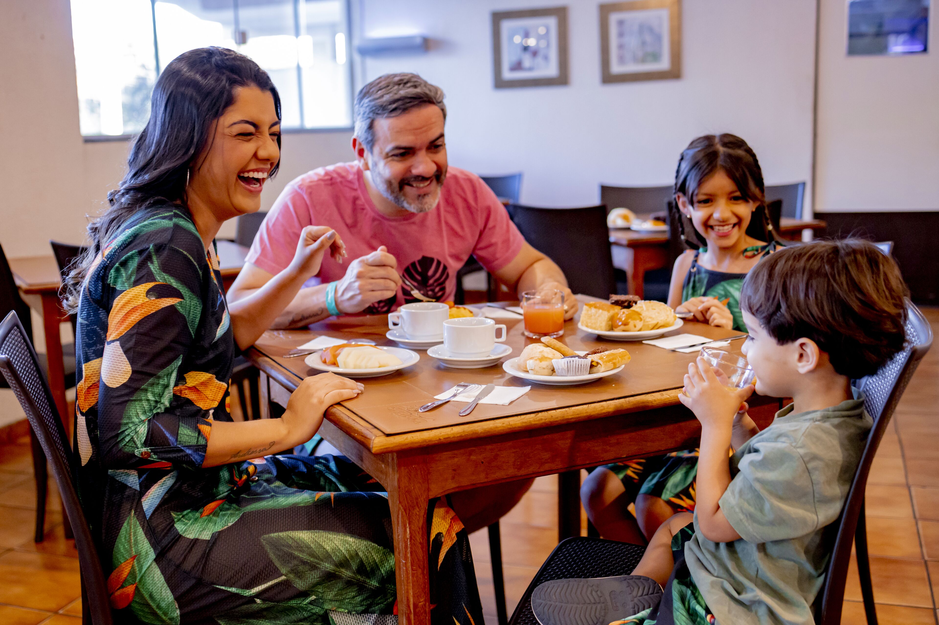 A family dining at a wooden table with plates of food, cups, and a glass of orange juice.