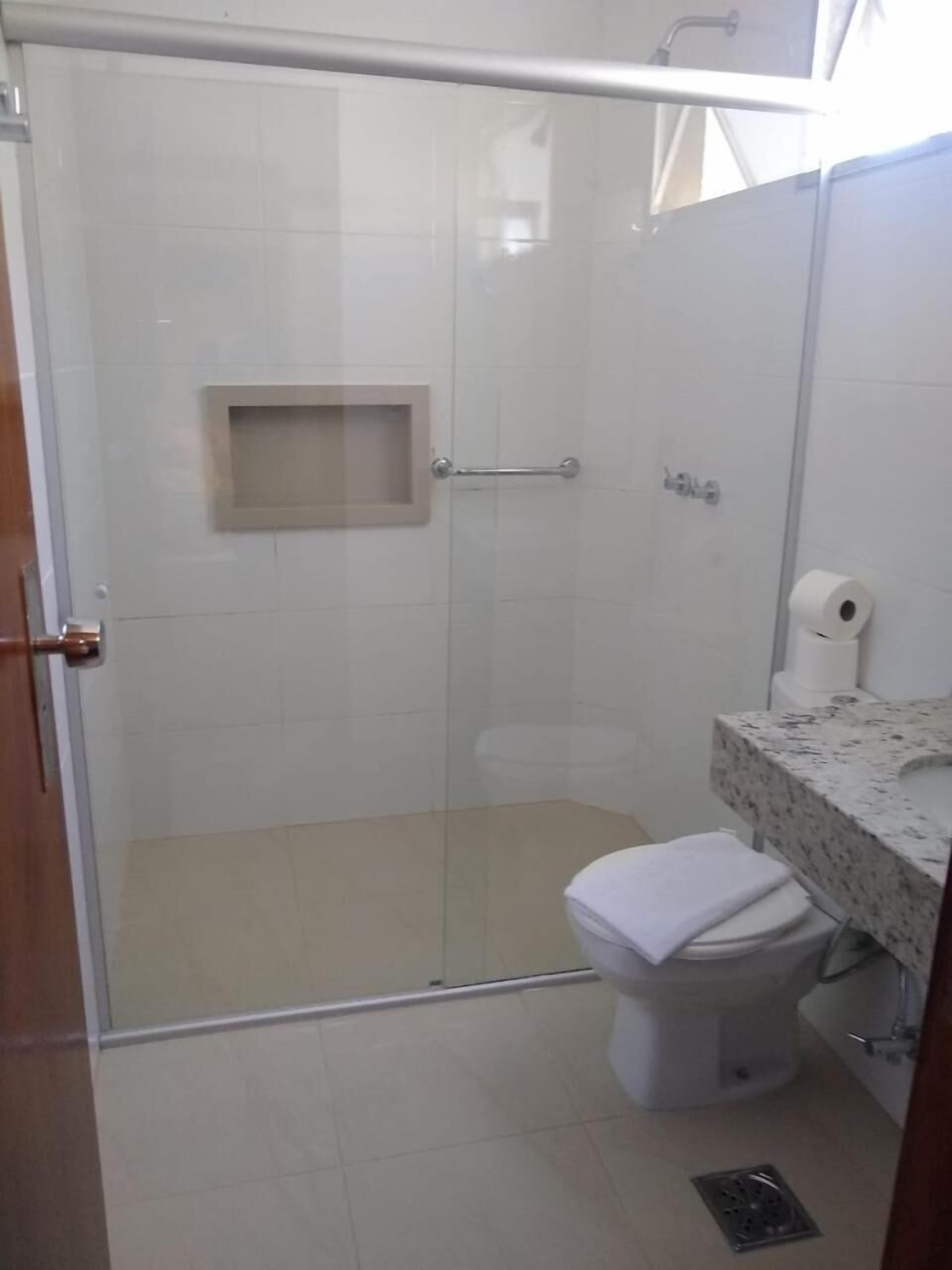 A bathroom with a glass-enclosed shower, a toilet, and a marble sink.