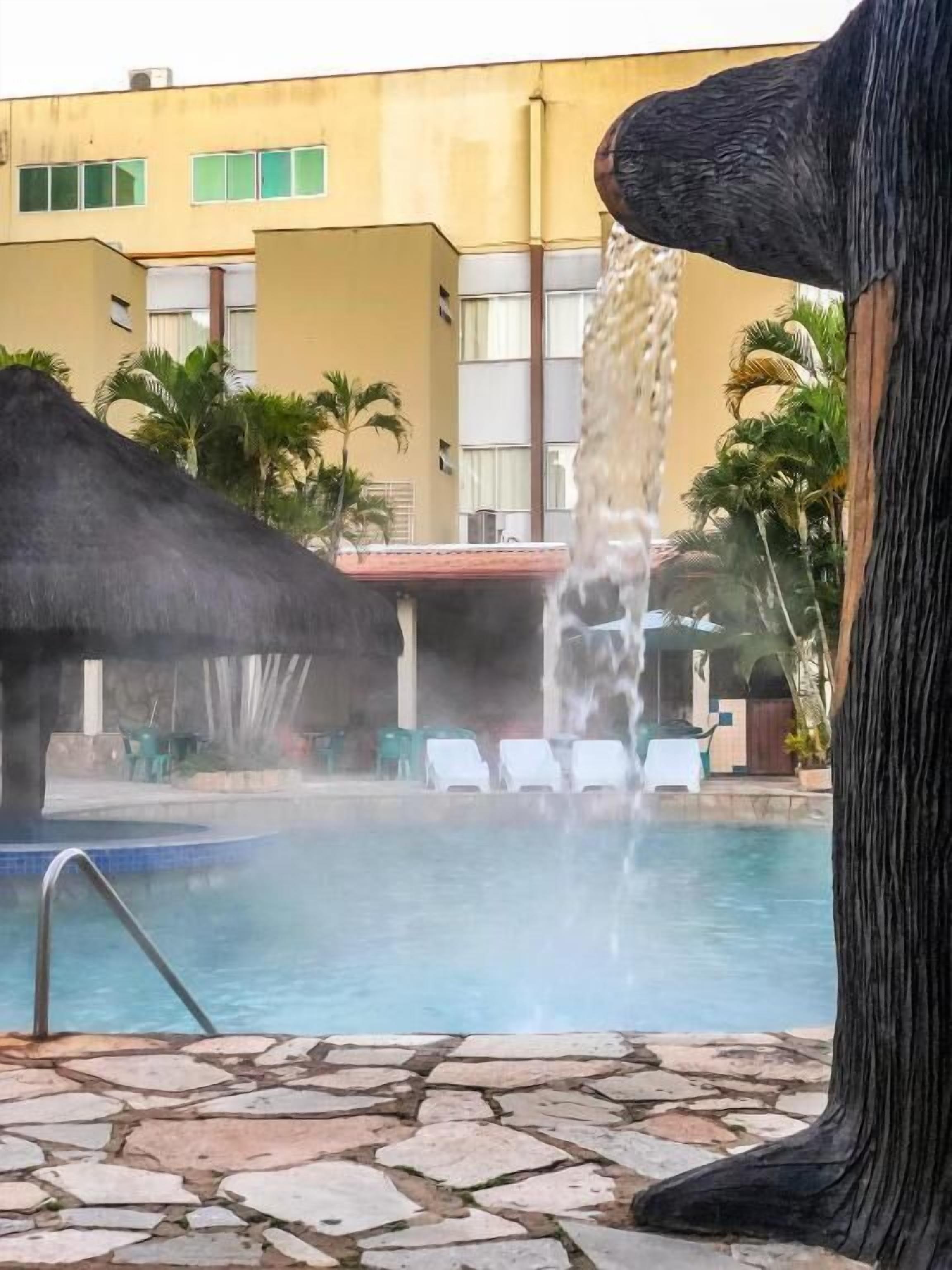 A pool area with a stone-tiled deck, lounge chairs, and a water feature.