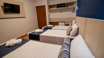 A hotel room with two beds, a TV mounted on the wall, a small desk, and a wardrobe.