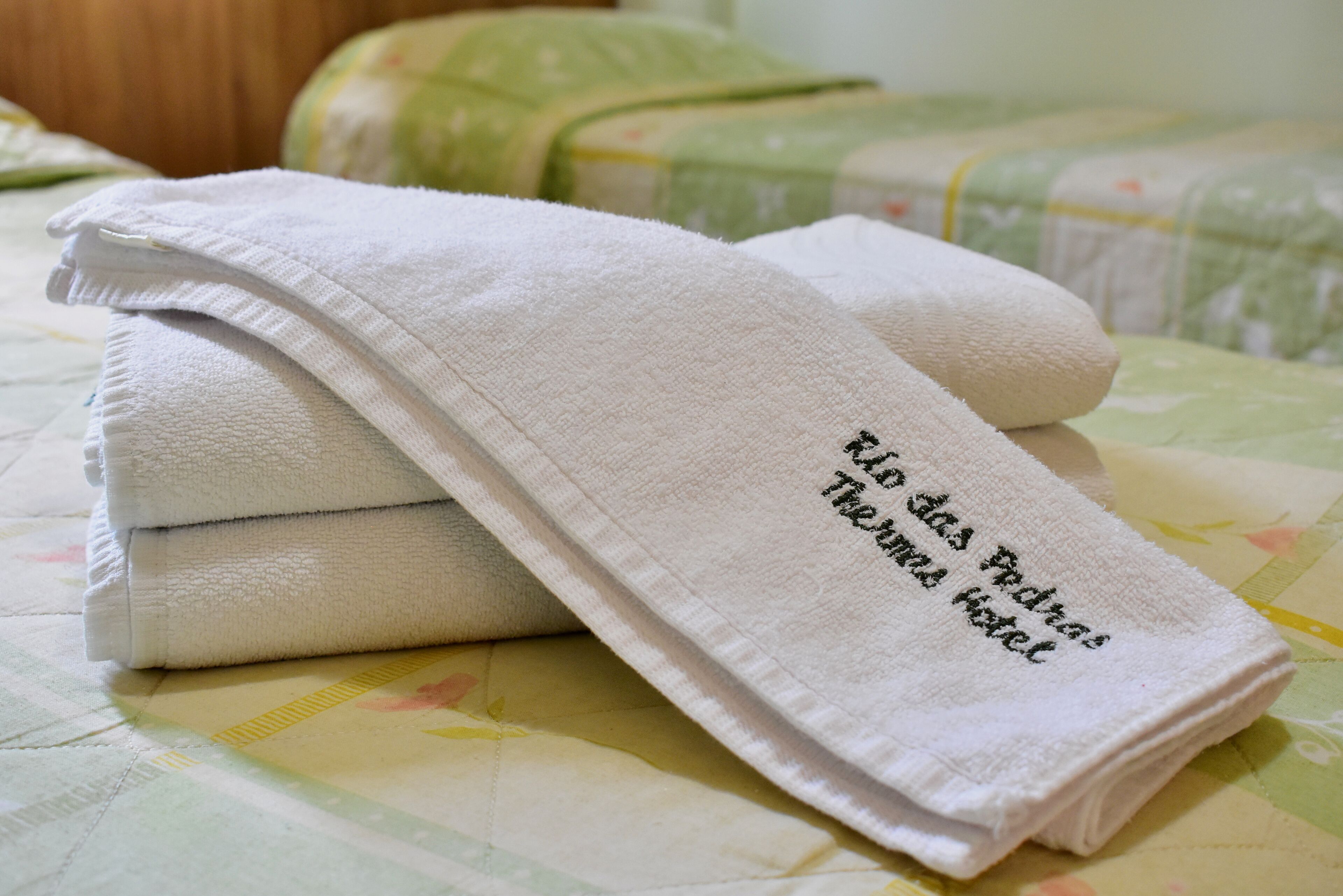 Une serviette blanche, soigneusement pliée et ornée d’un motif, est posée sur un lit recouvert d’une couvre-lit à motifs floraux.