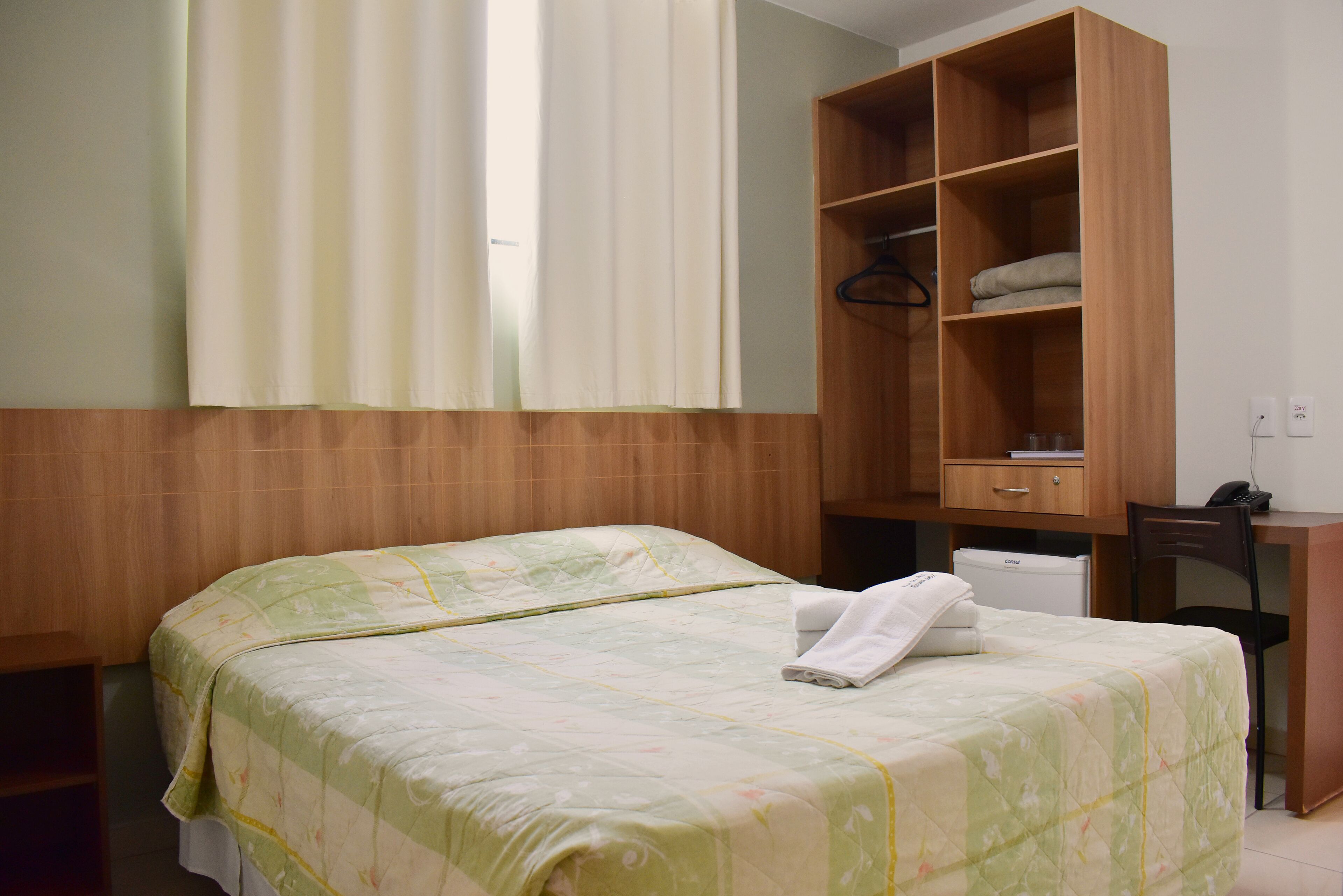 Una habitación de hotel con una cama, un armario de madera, un escritorio y una silla.