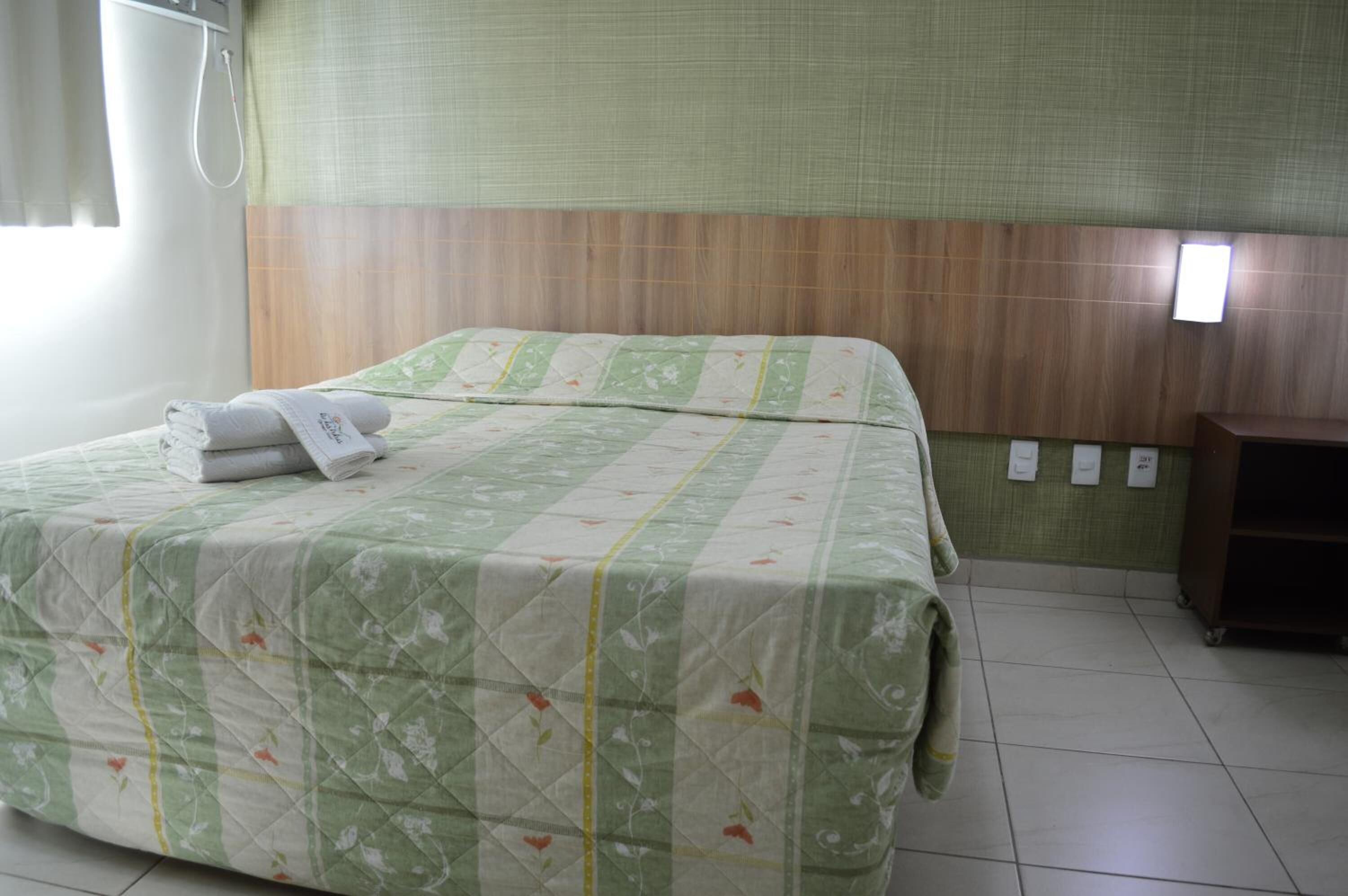 A neatly made bed with a floral bedspread, a wooden headboard, and a small wooden nightstand.