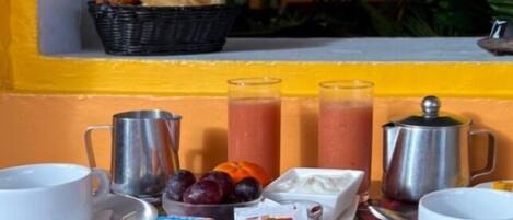 A breakfast setup with a table, cups, a pitcher, a bowl of fruit, and a basket of bread.