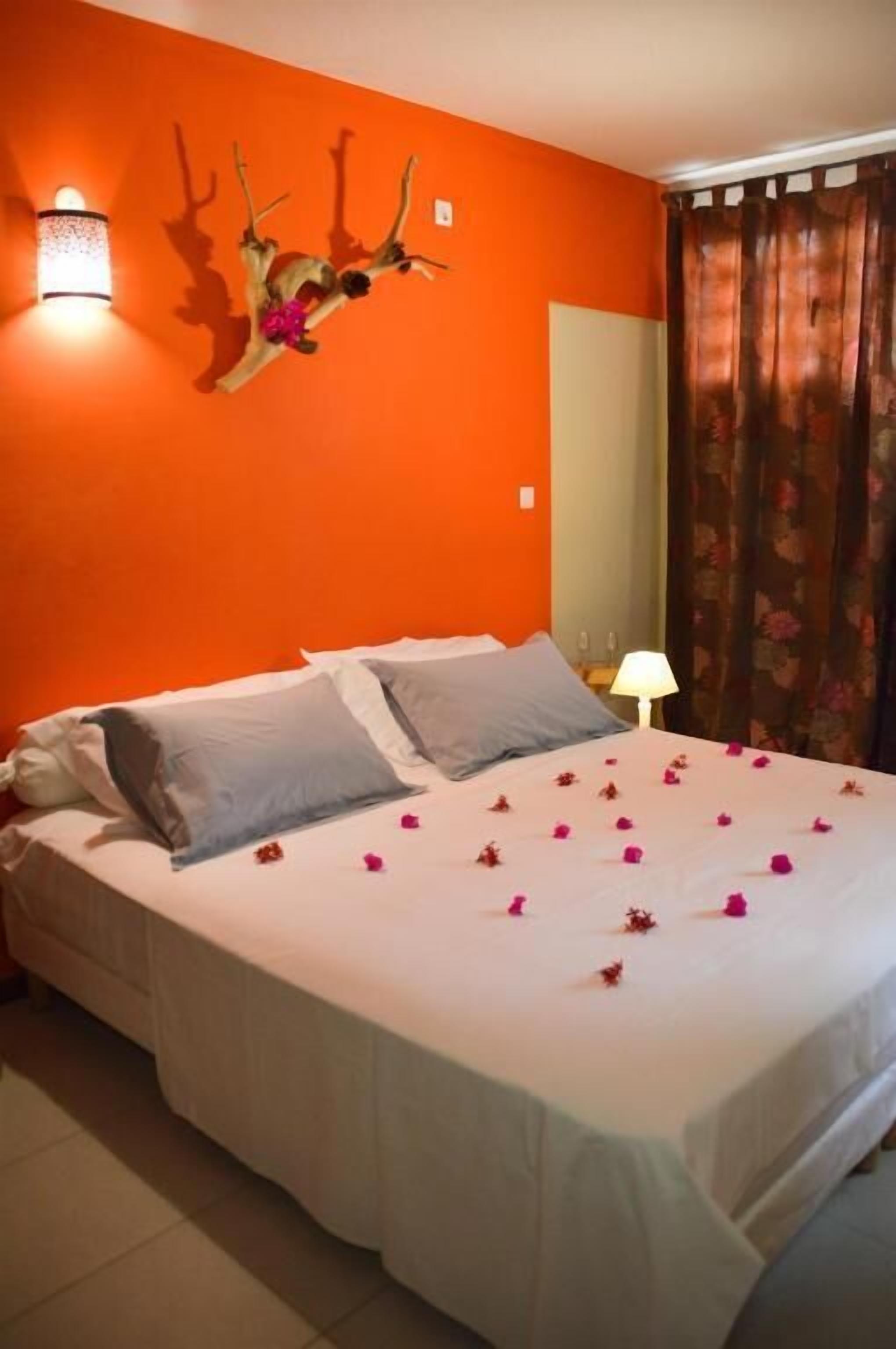 Un letto con biancheria bianca e fiori rosa, una decorazione a testa di cervo appesa al muro e una lampada.