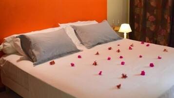 Un letto con biancheria bianca e fiori rosa, una decorazione a testa di cervo appesa al muro e una lampada.