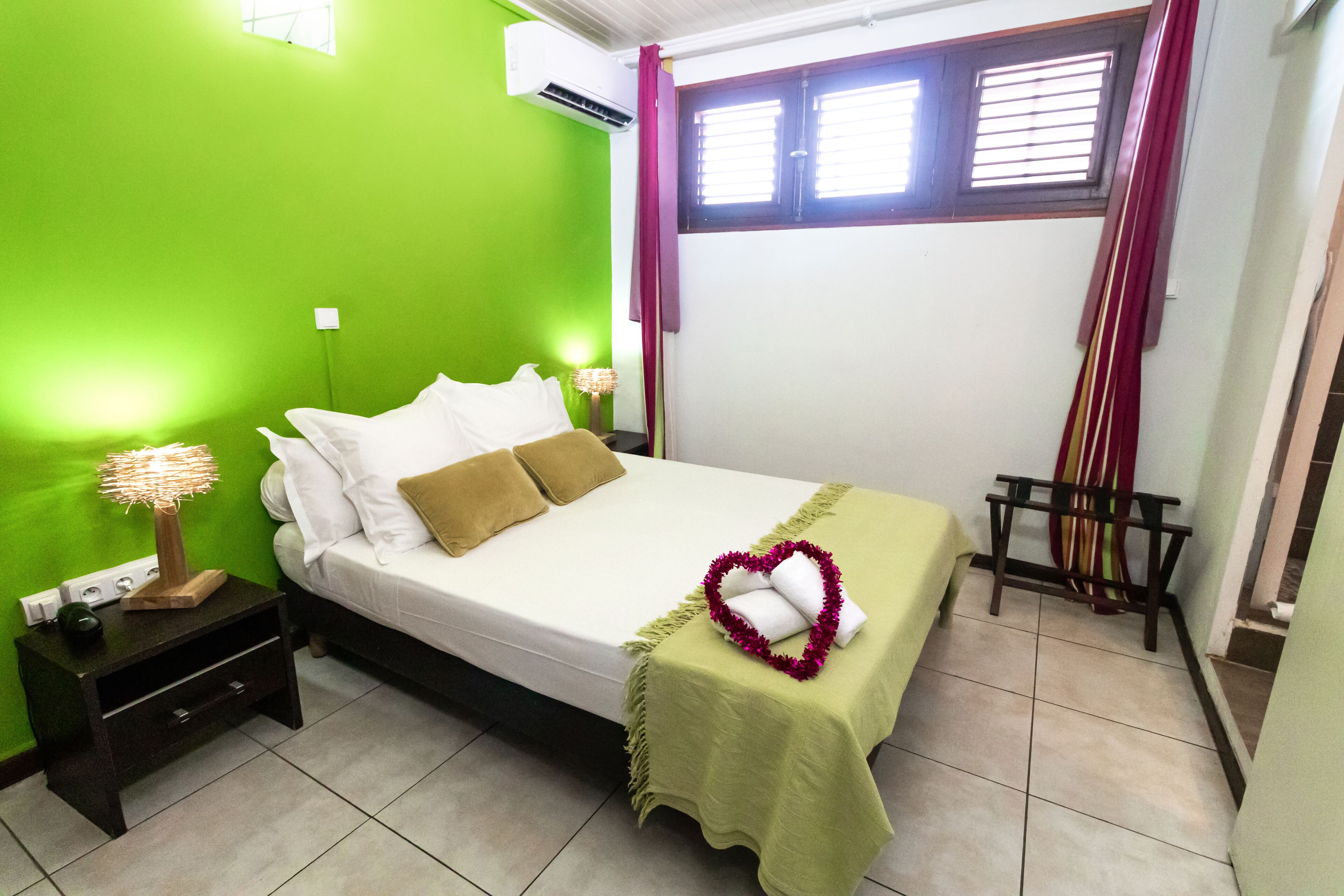 Una camera da letto ordinata con un letto, un comodino, una lampada e una decorazione a forma di cuore.