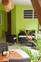 Una habitación con pared verde, muebles de mimbre, una mesa de madera con bebidas y una ventana con persianas.