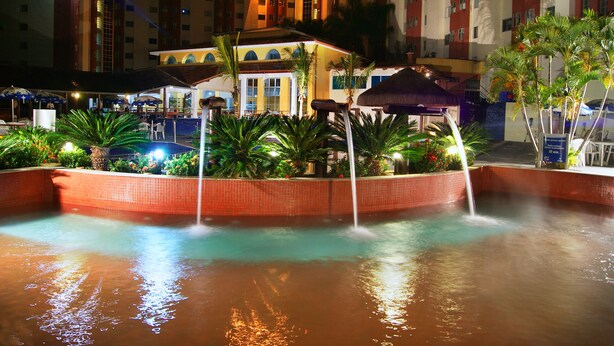 Un espace piscine d’hôtel agrémenté de plusieurs éléments aquatiques, notamment une fontaine centrale et des jets d’eau disposés tout autour.
