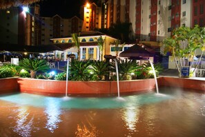 Een zwembadgedeelte van een hotel met diverse waterattracties, waaronder een centrale fontein en omliggende waterstralen.