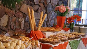 Une table de buffet garnie de différents pains et pâtisseries, un mur en pierre et une fenêtre décorée de fleurs.