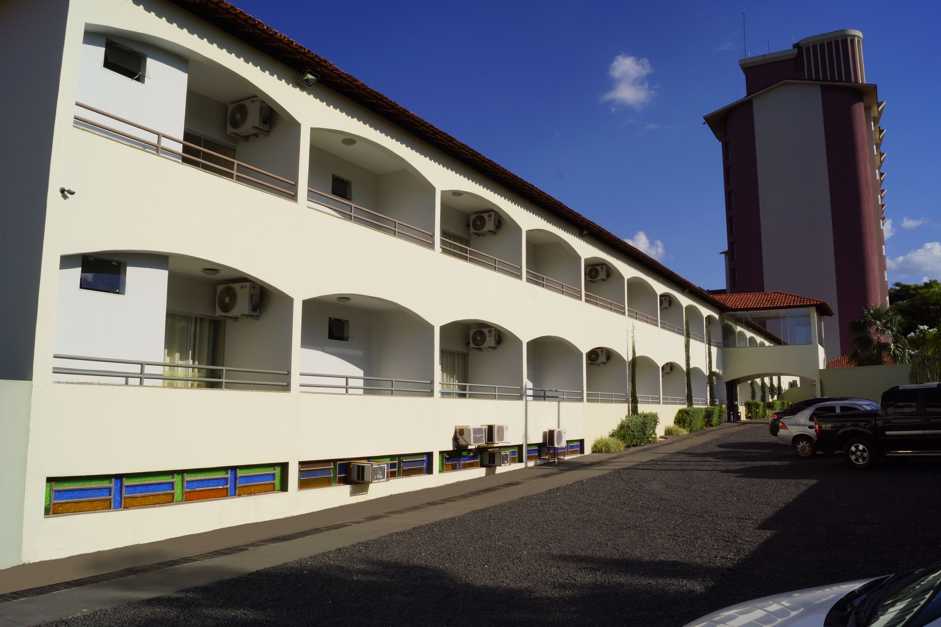 A multi-story building with balconies, air conditioning units, and a parking area.