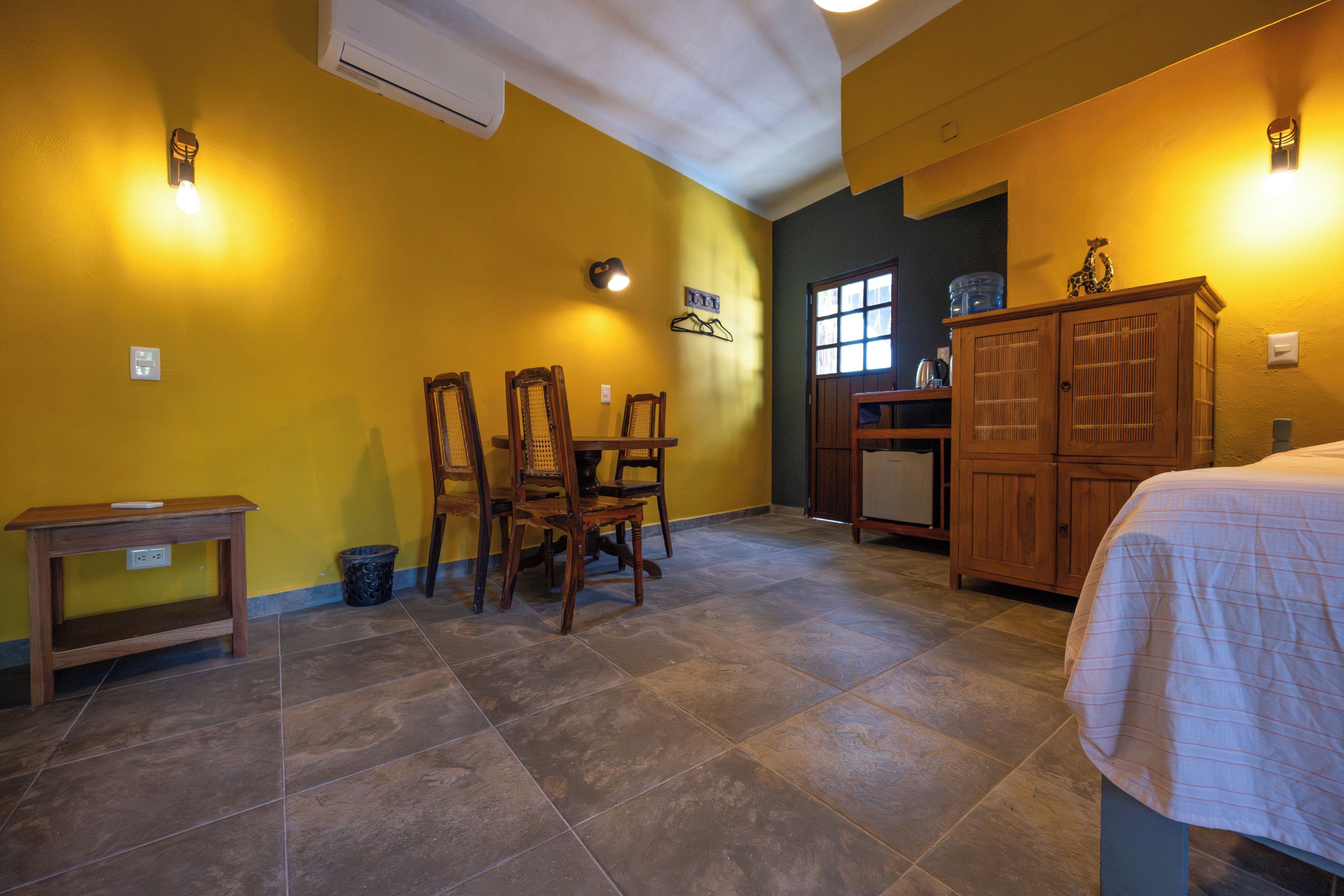 A room with a dining area, a bed, a cabinet, and a window.