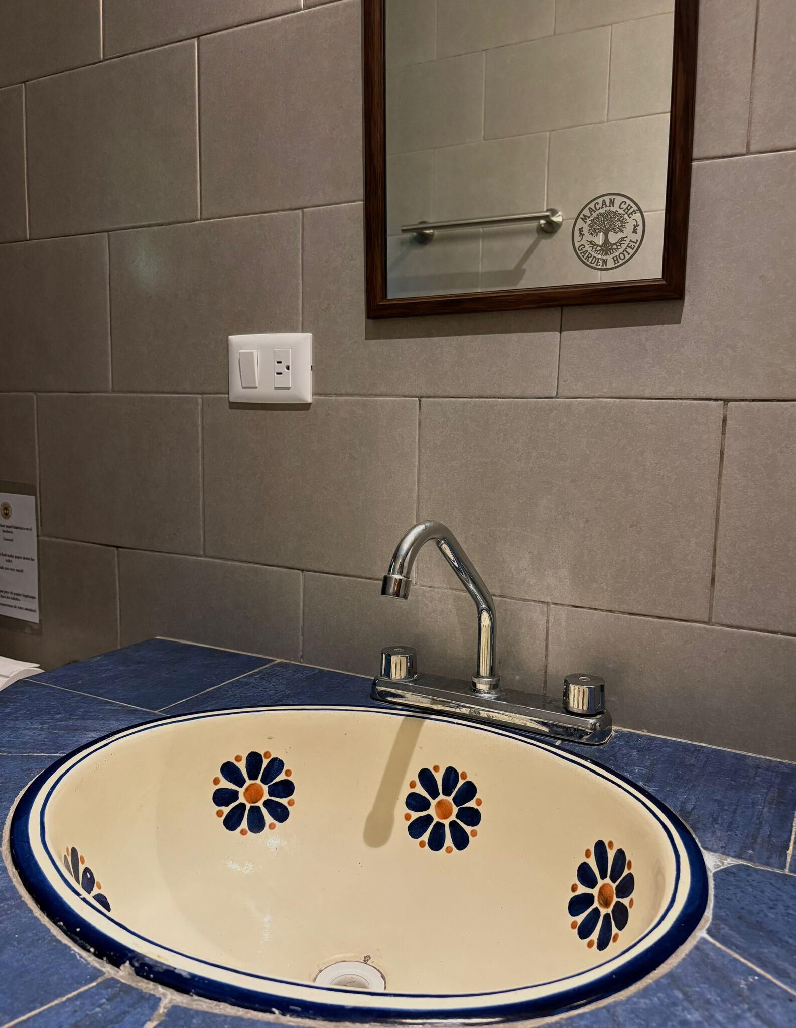 A bathroom with a beige sink featuring blue and orange floral patterns, a chrome faucet, and a mirror with a wooden frame.