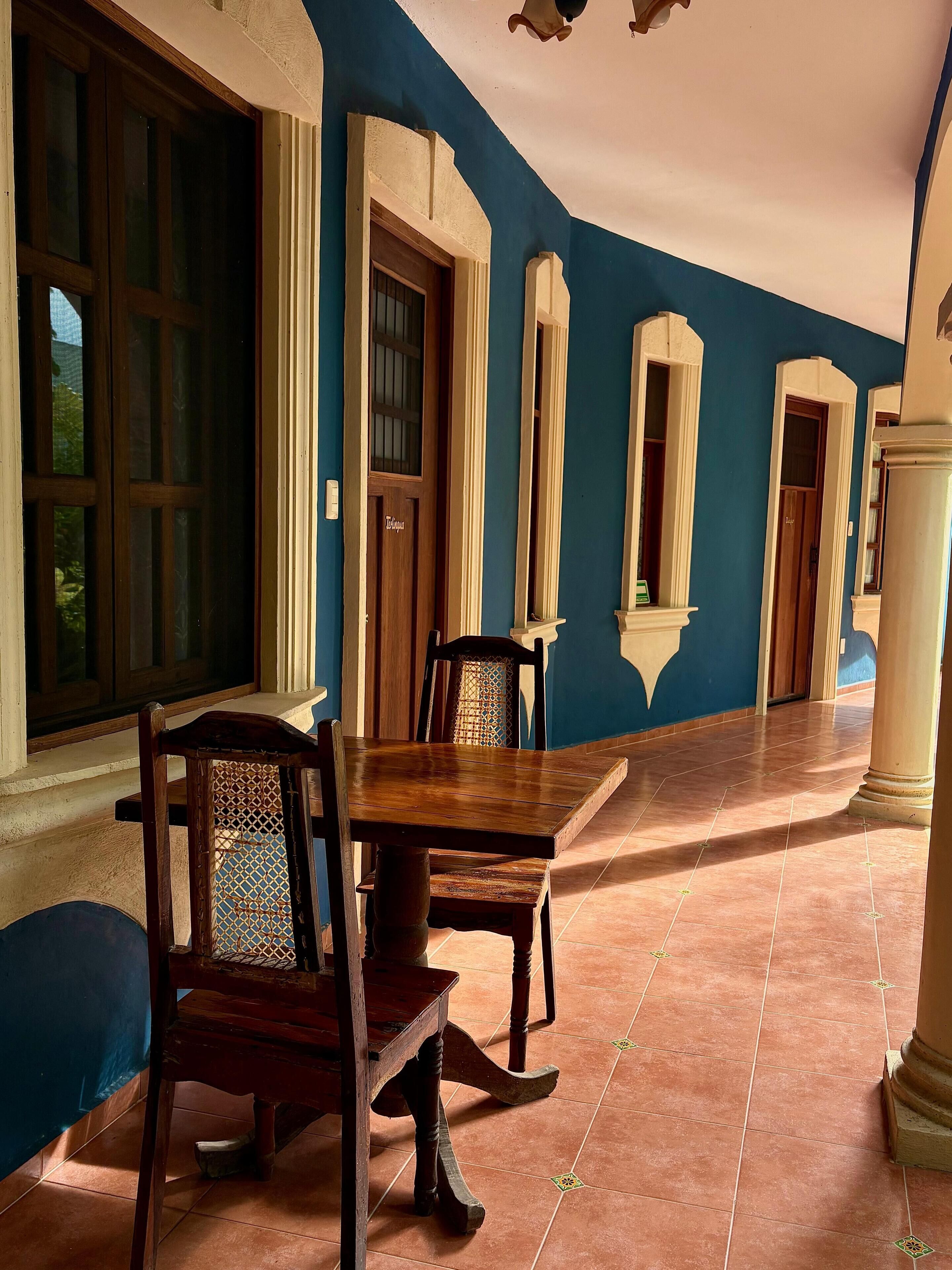 Une pièce avec une table et des chaises en bois, une grande fenêtre et un mur bleu.