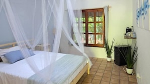 A bedroom with a bed under a white canopy, a window with a view of greenery, and a tiled floor.