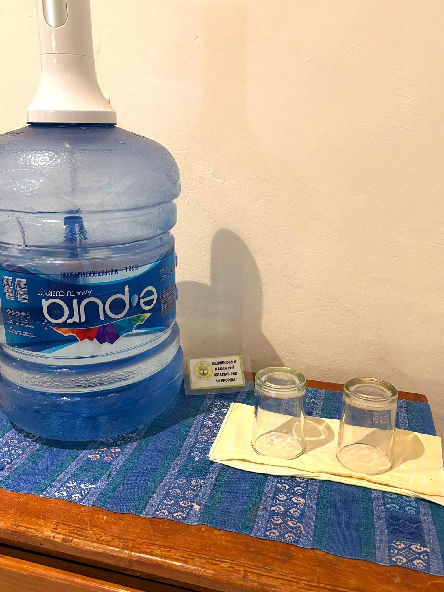 A large water dispenser, two shot glasses, and a welcome sign on a table.