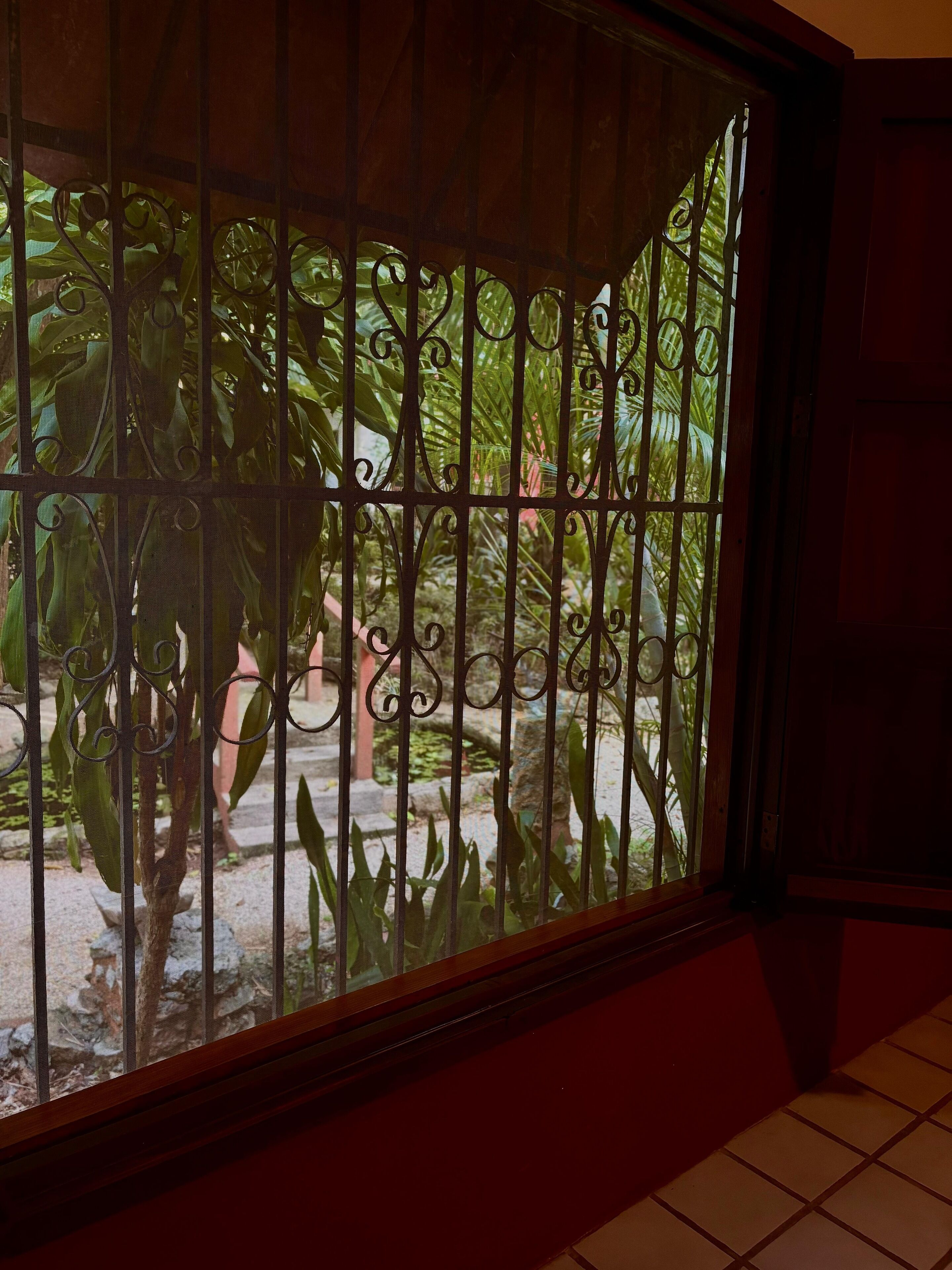Una ventana con barrotes metálicos decorativos y vistas a un jardín con diversas plantas.