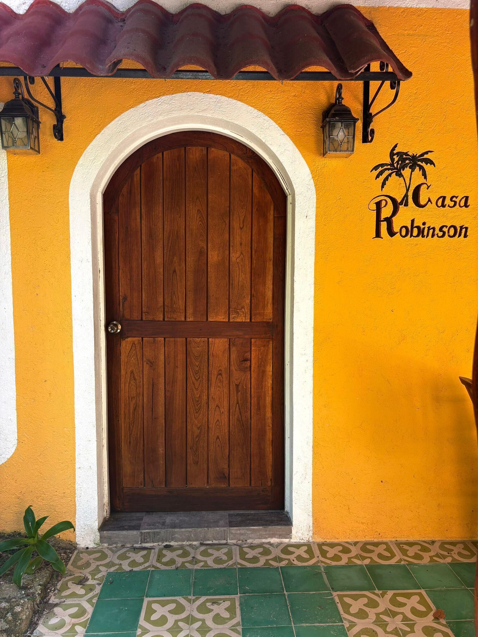 A wooden door with an arch, a tiled entrance, and a wall with a logo and text.