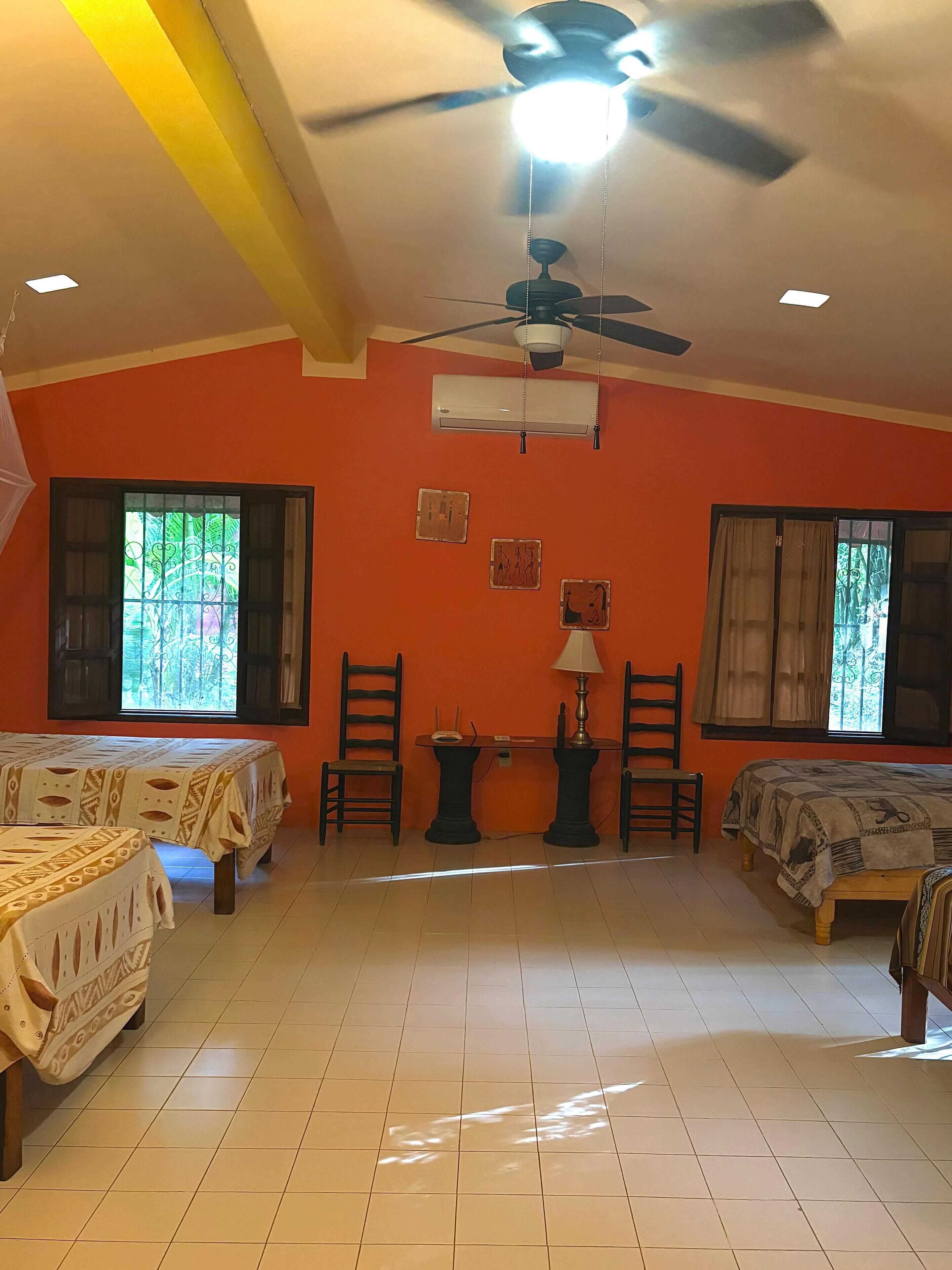 Una habitación con dos camas, ventilador de techo, aire acondicionado y una mesa con sillas.
