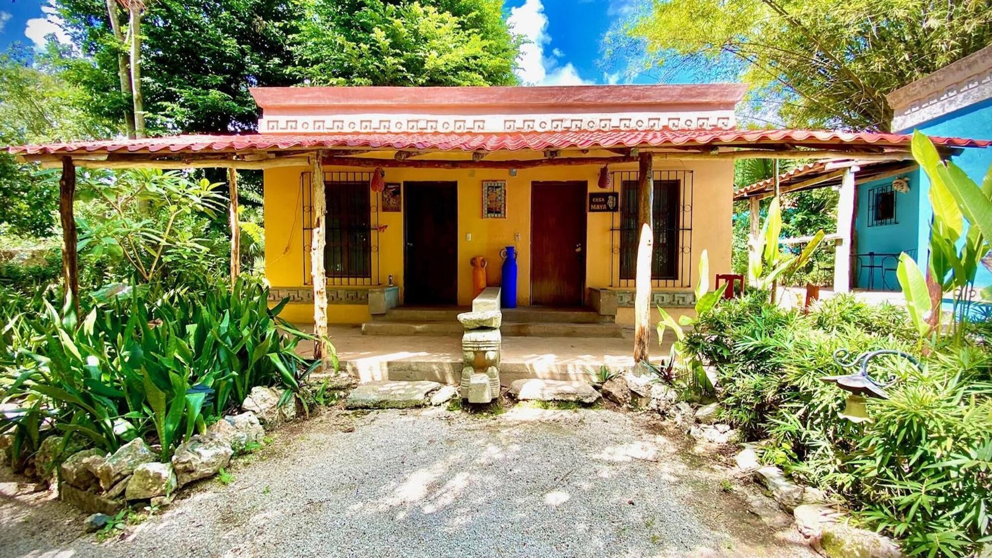 A yellow building with a red roof, a stone staircase, and a small garden with rocks and plants.