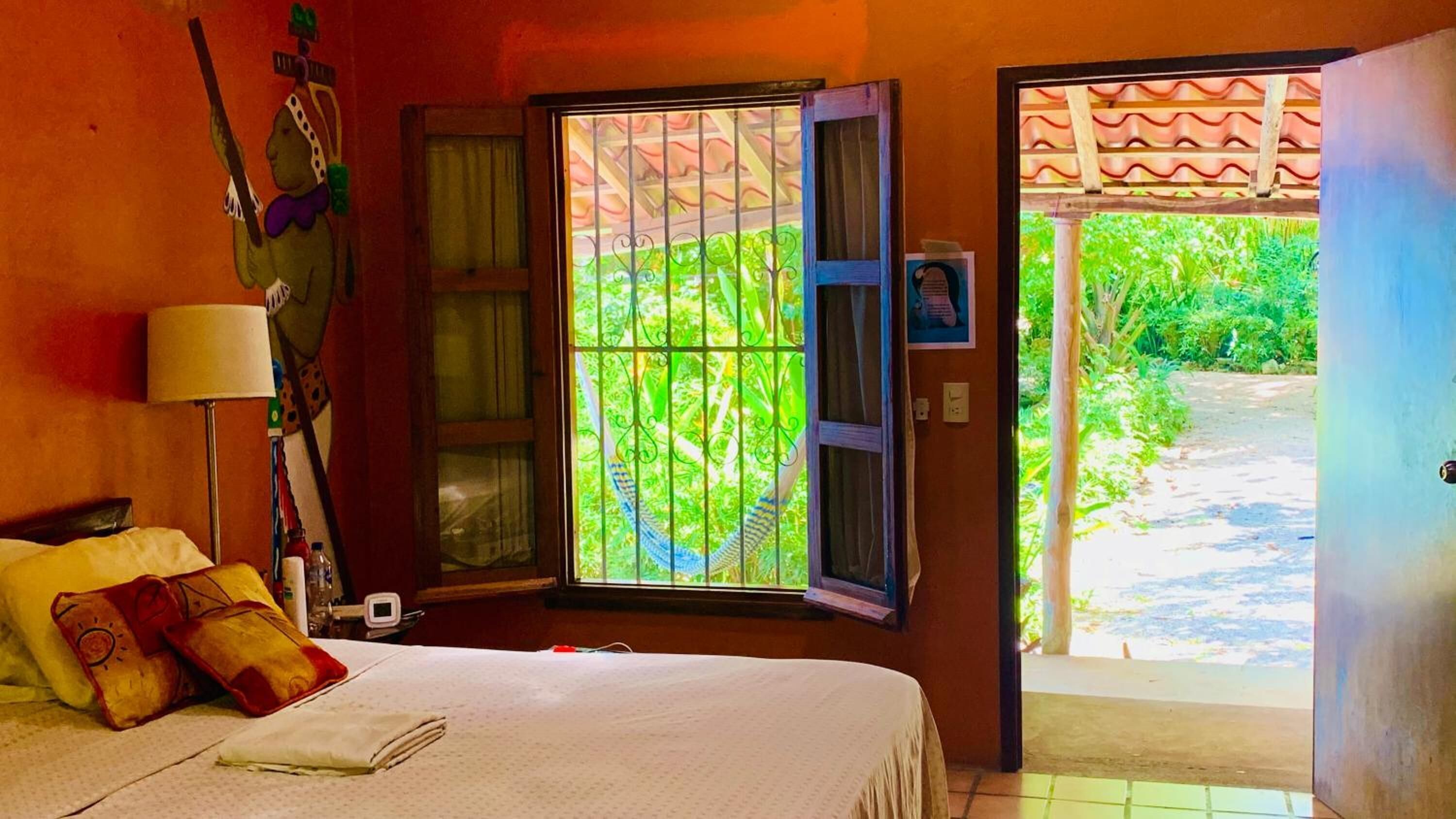 A bedroom with a bed, a window with bars, a door leading outside, and a wall with a decorative item.