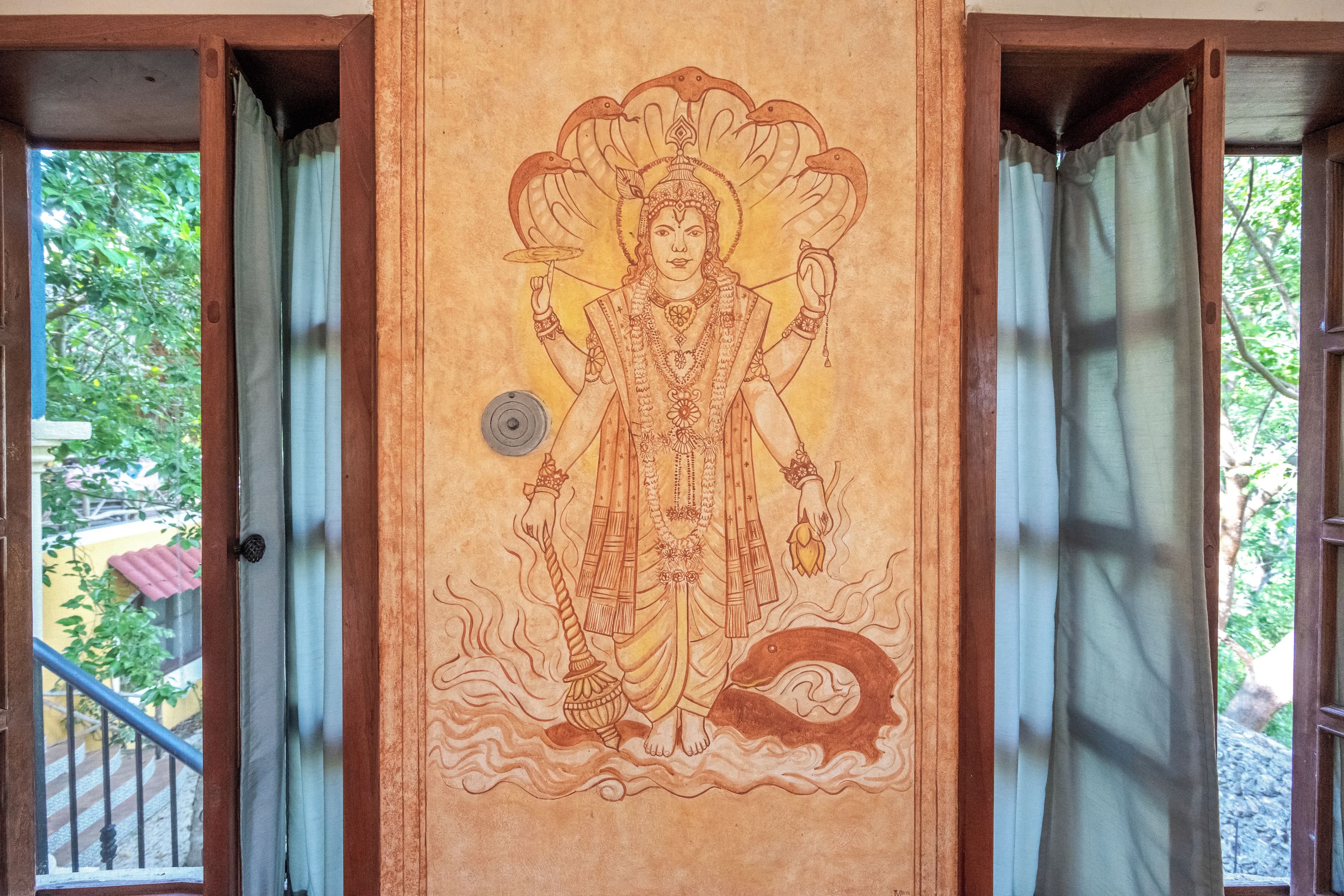 A door with a religious mural, a metal doorbell, and a view of greenery outside.