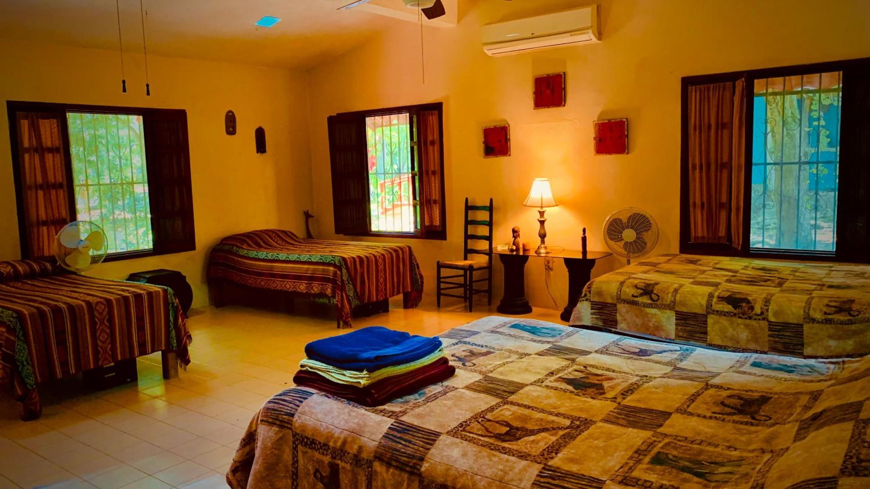 A hotel room with two beds, a sitting area with a table and chairs, and large windows with curtains.