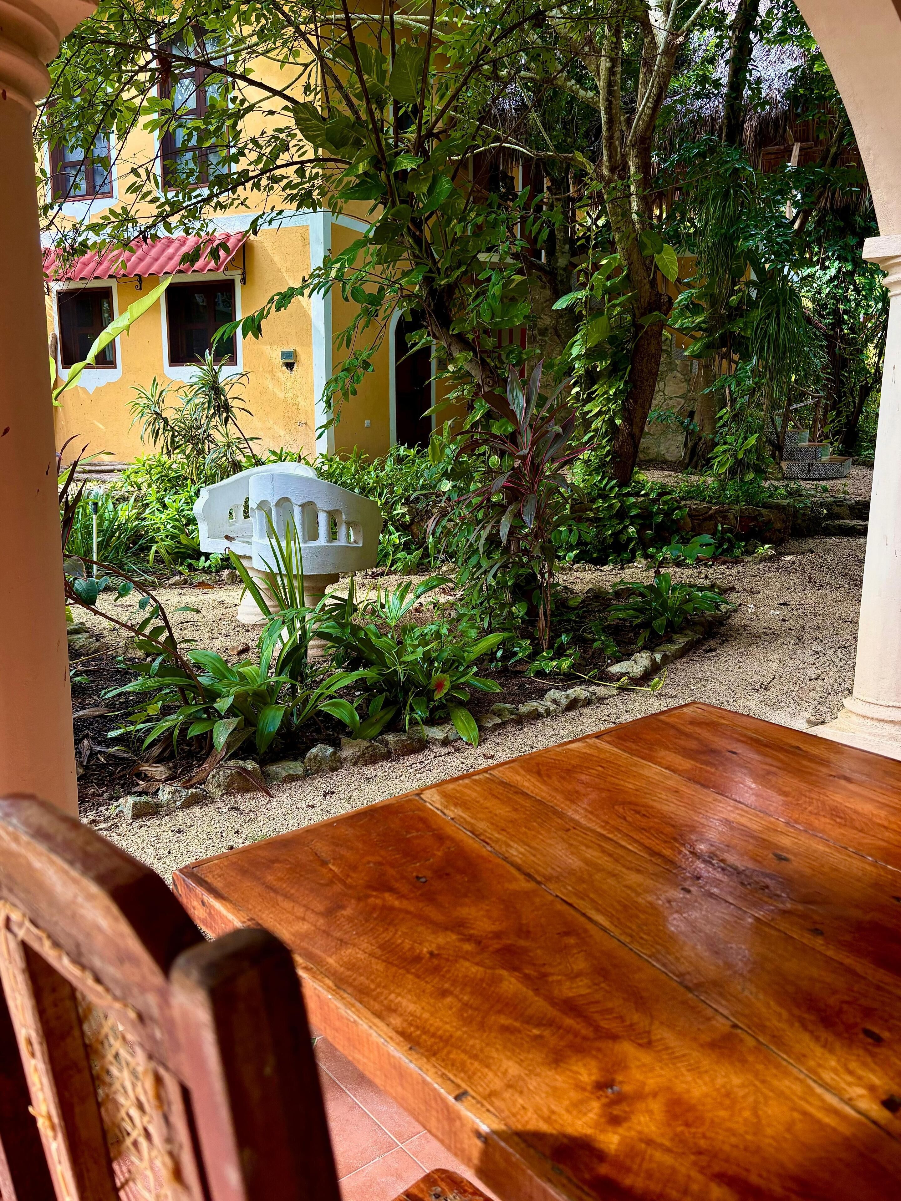 A wooden table and chairs in a courtyard with a yellow building in the background.