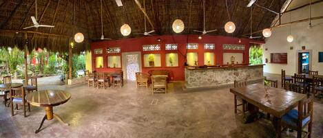 A restaurant with a thatched roof, wooden furniture, and a stone counter.