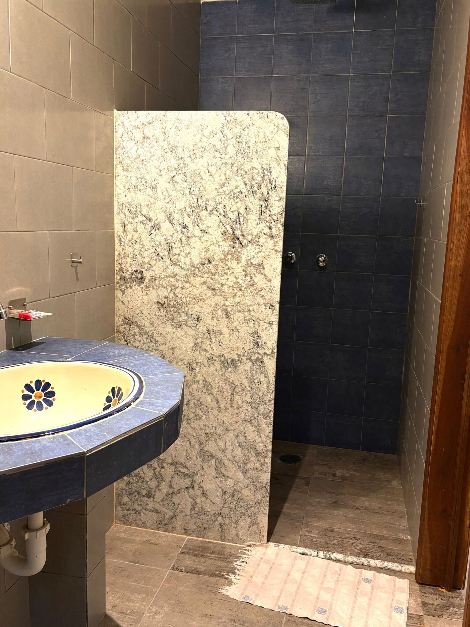 A bathroom with a marble sink, dark tiled walls, and a shower area.